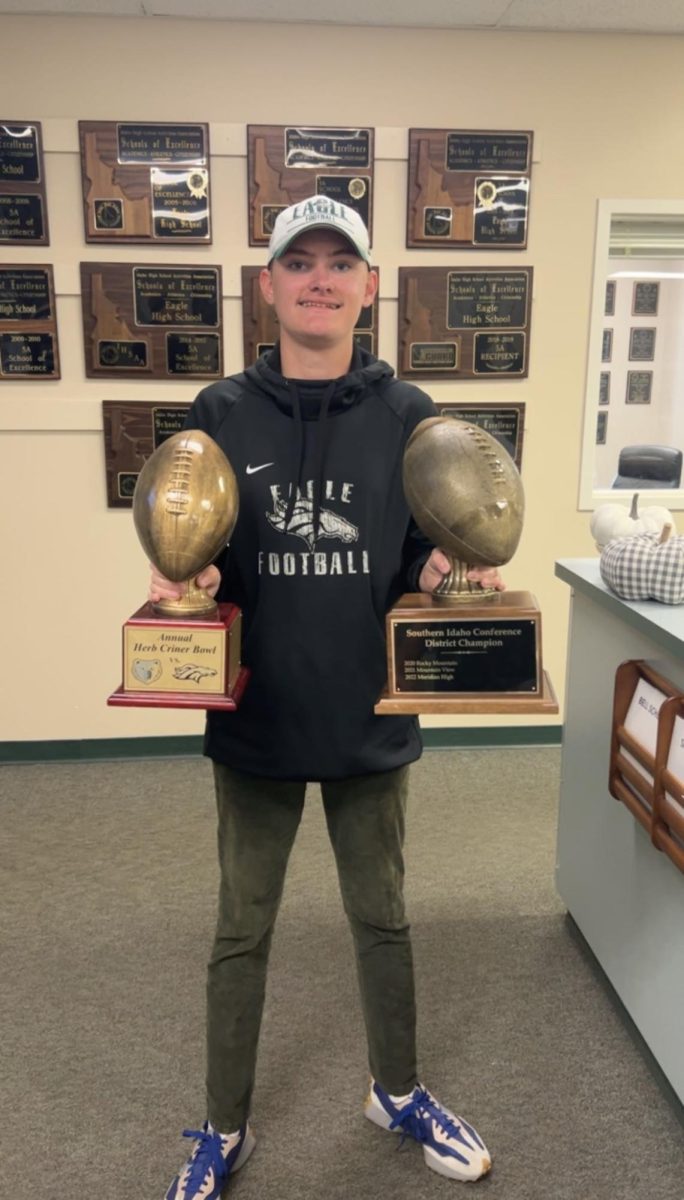 Senior Ethan Evans holds the Herb Criner trophy and the Southern Idaho Conference District Champion trophy won by the varsity football team at Eagle High. Evans works as an equipment manager for the football team.