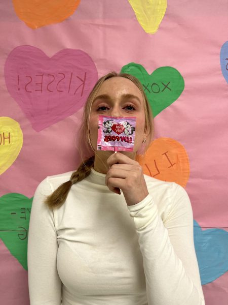 Sophomore Savannah Flake holds up a heart-themed candy in front of one of the Valentine’s Day posters created by the Eagle High student council. Students celebrate Valentine’s Day by giving gifts to or spending time with their loved ones.  