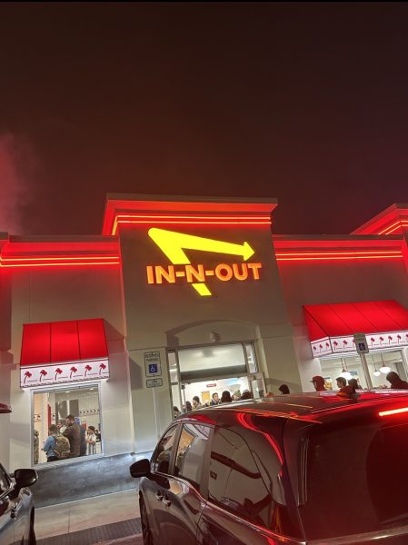 The iconic In-N-Out sign shines bright at night. Customers of the restaurant wait in long lines for a tasty meal. 