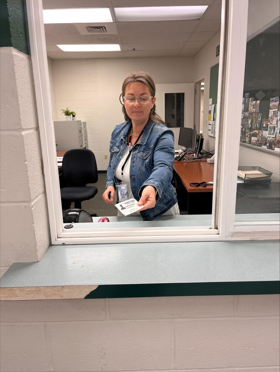 Staff member Naomi Wolff hands a student a tardy late slip. Students must get a tardy late slip from the attendance window when they are 10 or more minutes late, and this will count as two tardies.