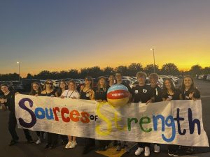 Sources of Strength members hold their sign after the homecoming parade during halftime of Eagle High’s football game. They spread positivity with their smiles.