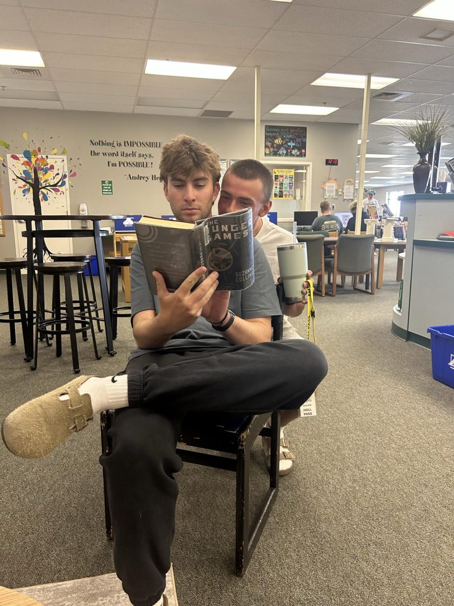Seniors Beau Saur and Brady Ford read a “Hunger Games” book in the Eagle High library. The Eagle High library has a large selection of dystopian books, such as “The Hunger Games.”