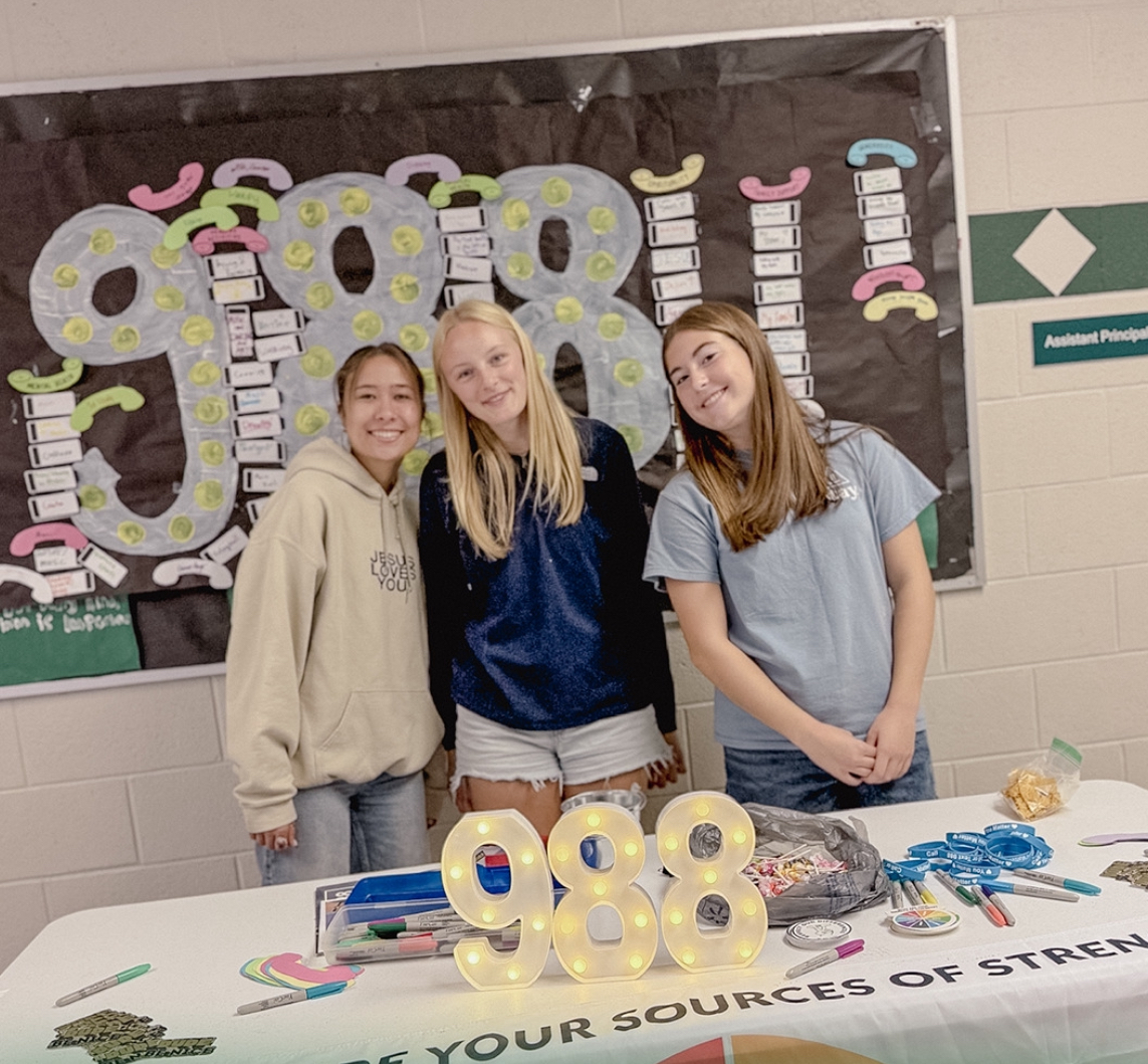 Sophomore Hannah Lloyd, sophomore Camille Krochmal and sophomore Emily McAllister represent Sources of Strength in the Eagle High school cafeteria. They are bringing awareness to Suicide Prevention Month with the suicide hotline displayed and illuminated on their table.