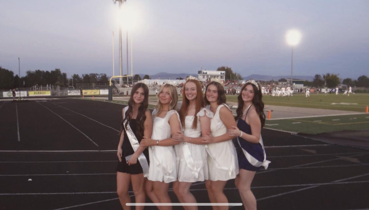 Freshman Rylee Schmidt, junior Evelyne Whiting, seniors Audrey Baxter, Bailey Kluksdal and sophomore Brooklyn Britton show off their homecoming dresses at the homecoming game. They receive crowns and sashes after winning homecoming royalty and are beaming with excitement at this opportunity. 