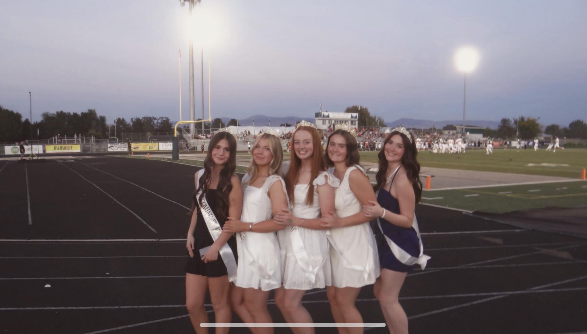 Freshman Rylee Schmidt, junior Evelyne Whiting, seniors Audrey Baxter, Bailey Kluksdal and sophomore Brooklyn Britton show off their homecoming dresses at the homecoming game. They receive crowns and sashes after winning homecoming royalty and are beaming with excitement at this opportunity. 