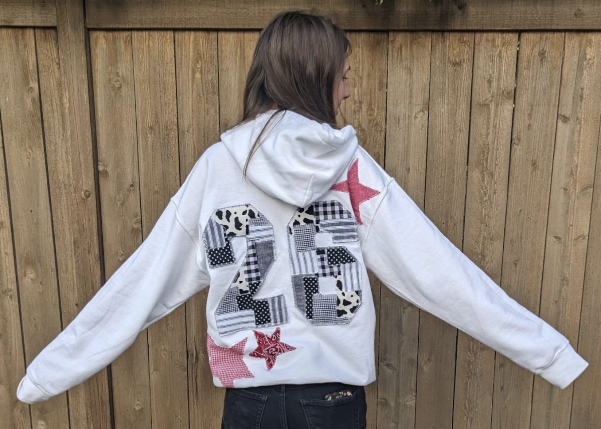 Senior Megan Baird shows her hand sewn hoodie design. She enjoys learning new things and she is having fun learning to sew to customize her personal style. She has designed this hoodie to feature her graduation year with a variety of fabric designs and patterns made into a 26.